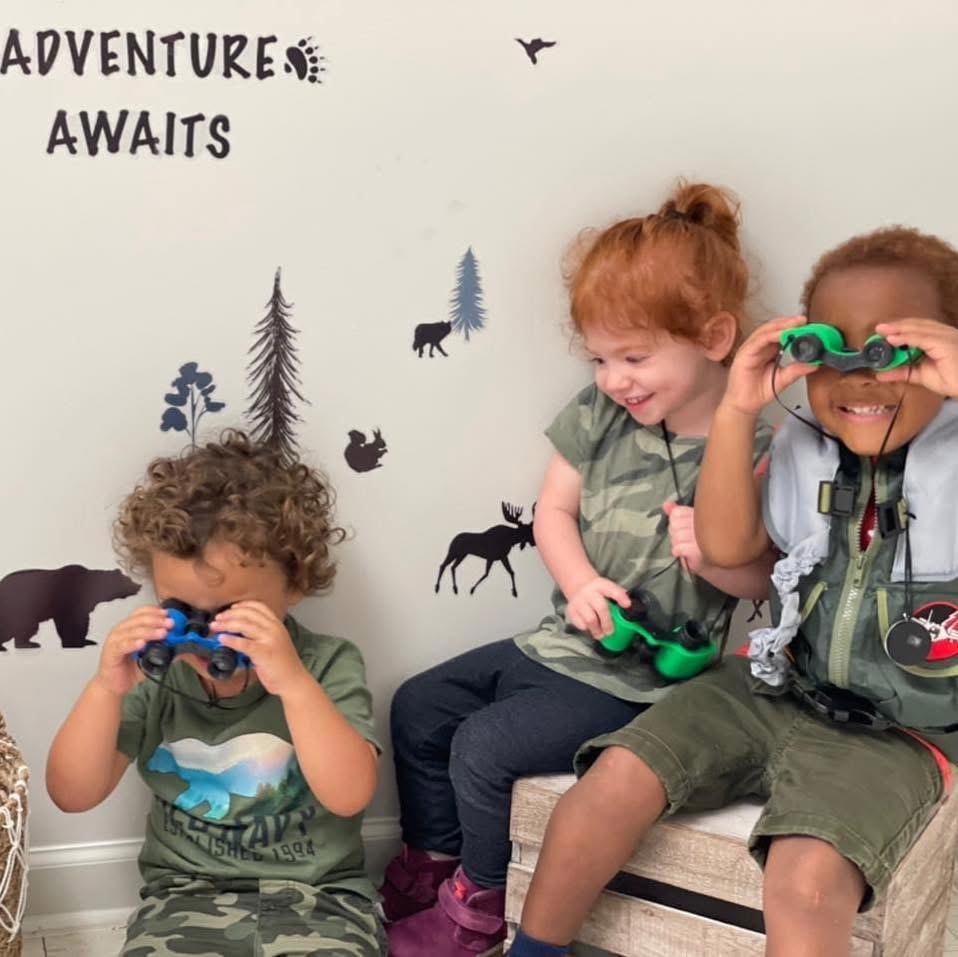 Three children with binoculars in front of Adventure Awaits wall decals