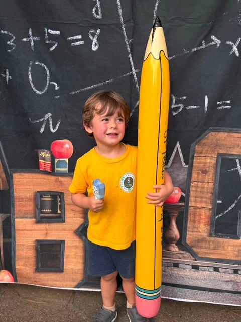 Boy hugging giant St. Peter's Academy pencil at back-to-school backdrop