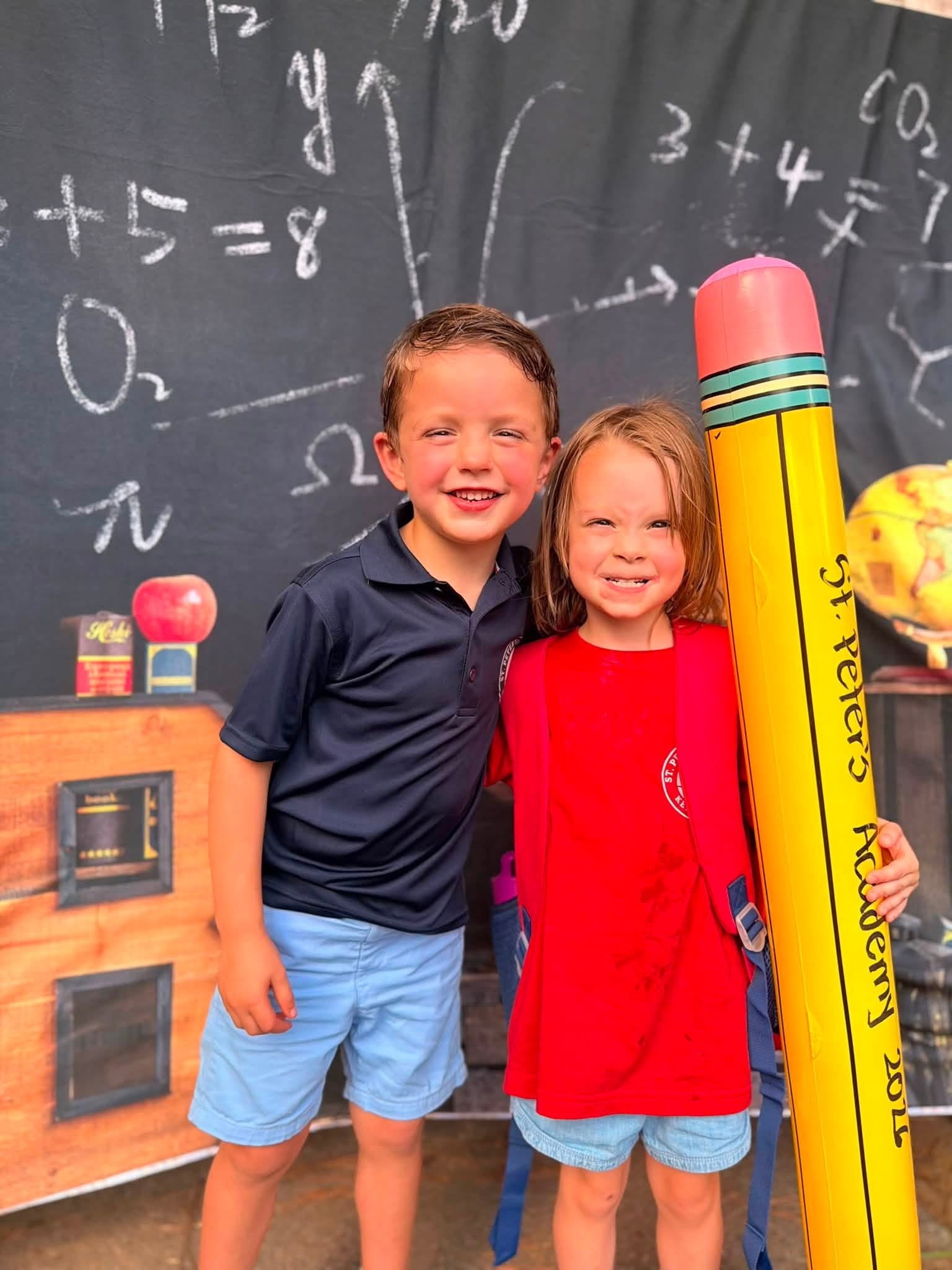 Two children posing with giant St. Peter's Academy pencil at back-to-school backdrop