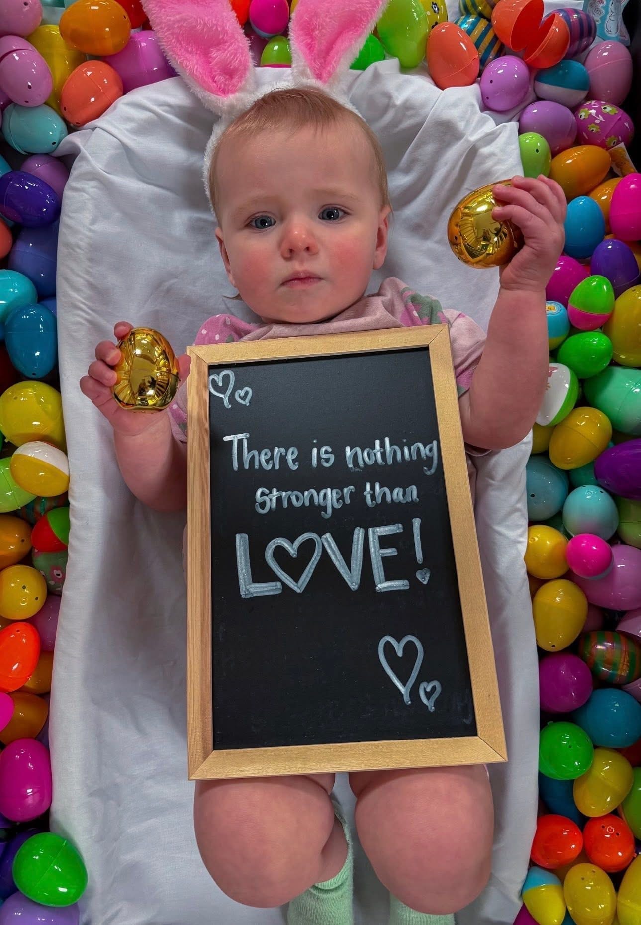 Baby with Easter bunny ears holding a chalkboard sign